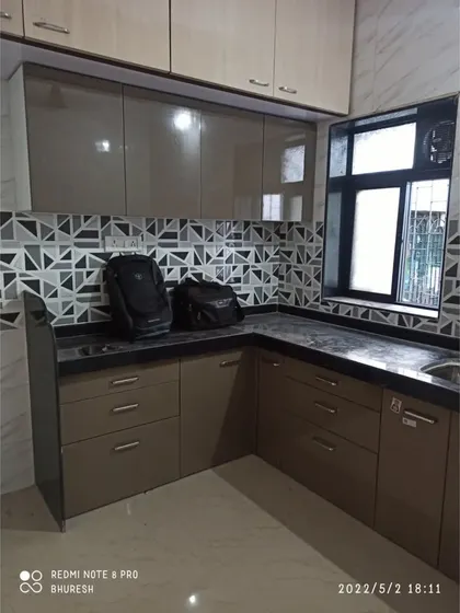 A compact L-shaped kitchen in Bhayander with high-gloss laminate cabinets and a bold geometric backsplash. Even in smaller spaces, a good design ensures ample storage and counter space.