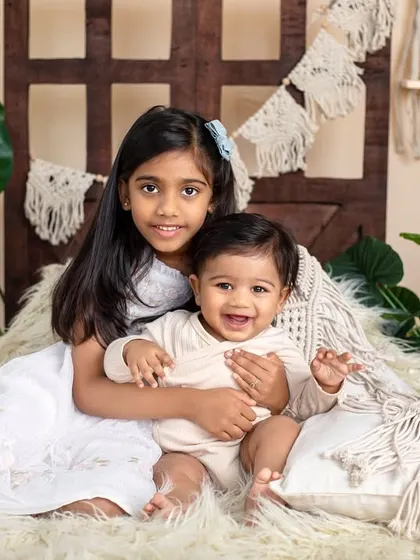 A big sister gives her baby brother a warm hug in our cozy, bohemian-style setup. The natural textures and colors create a calm and loving scene.