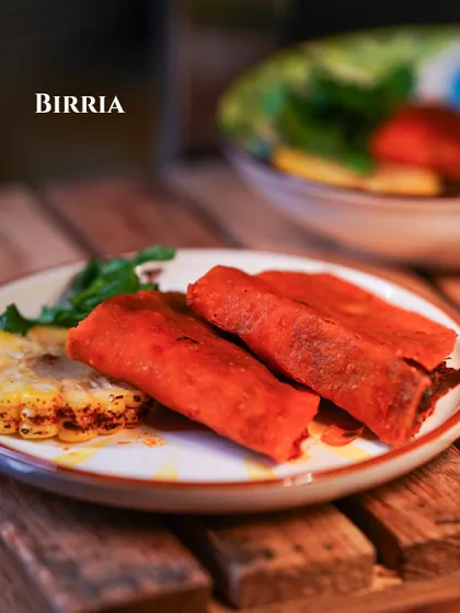 A plate of rich, slow-cooked Mexican Birria, served with a side of grilled corn.