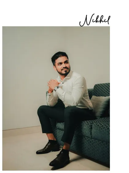 This is a relaxed, candid-style portrait of the groom. The soft, natural lighting and comfortable pose on the sofa create a moment that feels authentic and unforced, capturing his personality before the main event.