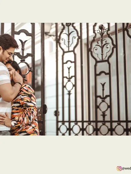 A tender and intimate pre-wedding moment, framed by the elegant ironwork of a gate.
