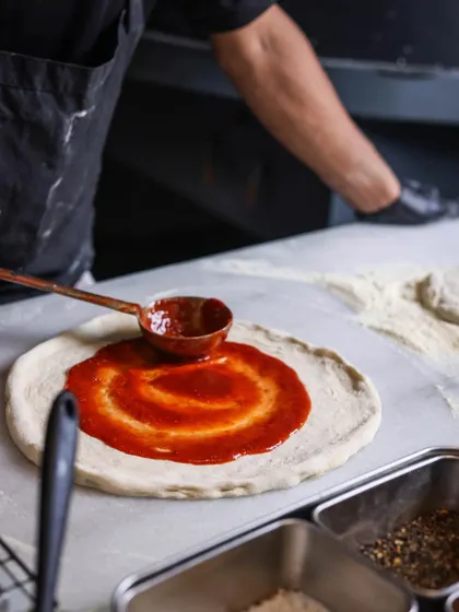 The secret is in the sauce. A swirl of rich, red tomato sauce on a fresh dough base is where every great pizza story begins.