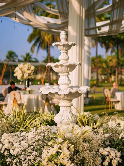 A classic three-tiered white fountain serves as a central feature in the garden, surrounded by a bed of white flowers. This timeless element adds a touch of European garden elegance to the event.
