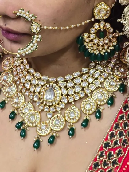 A close-up of a beautiful Pachi Kundan necklace with green bead drops, worn with a red lehenga. The detail in the Kundan work is clearly visible.