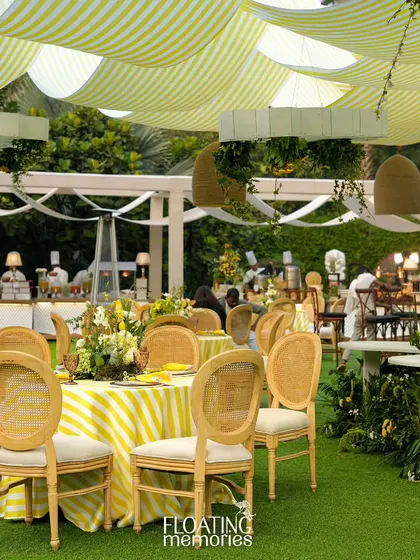 The elegant guest seating arrangement, with striped tablecloths and natural wood caned chairs, perfectly complements the sunny, garden-party vibe of this luxury baby shower.