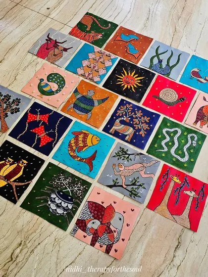 The full collection of 20 hand-painted and embroidered Gond art tiles laid out on the floor. Each square tells its own story with a unique animal or symbol, creating a vibrant tapestry of color and life.