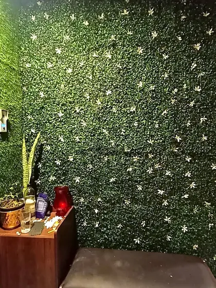 A close-up of a decorative artificial green wall panel with small white flowers. This type of panel is great for adding texture and a touch of elegance to any indoor space with zero maintenance.
