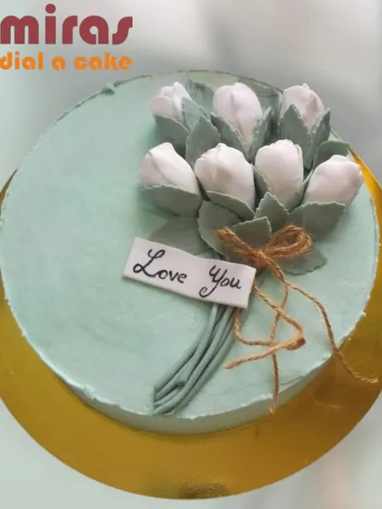A minimalist and heartfelt cake with a message of "Love You." The design features a simple bouquet of white tulips made from frosting, tied with a rustic twine bow.