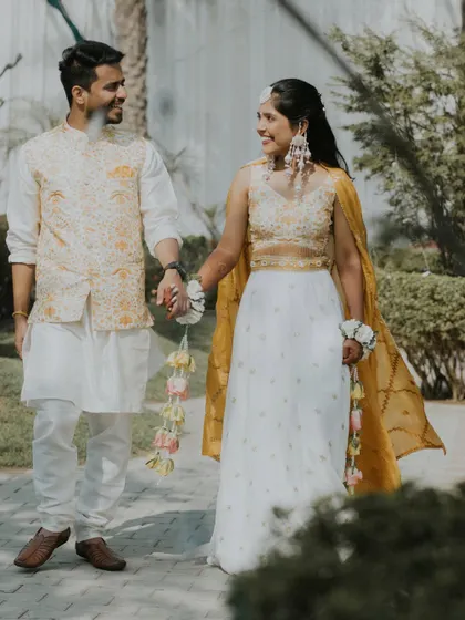A full-length portrait of Nikita and Akash walking hand-in-hand in their beautiful white and yellow Haldi outfits.
