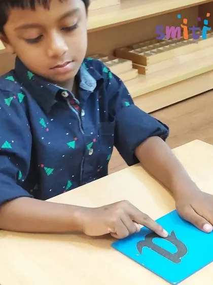 A boy traces a sandpaper letter with his fingers, feeling the shape as he says the sound. This tactile experience solidifies the connection between the symbol and its phonetic sound.