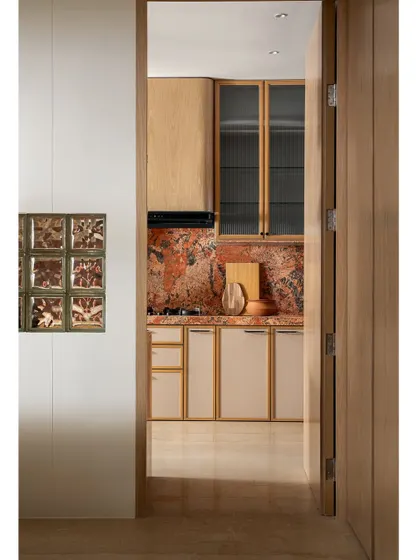 A view into the kitchen through the doorway, showing how the glass blocks on the outer wall allow light to filter in. The warm wood and bold marble create an inviting and visually interesting kitchen.