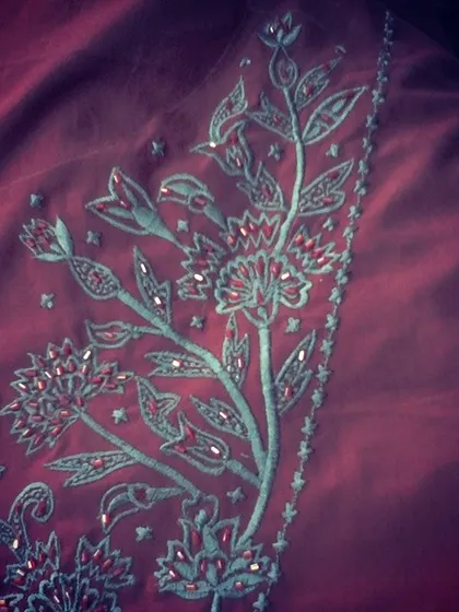 A detailed shot of floral embroidery on a rich maroon fabric. The combination of different stitches and subtle embellishments creates a beautiful, textured effect.