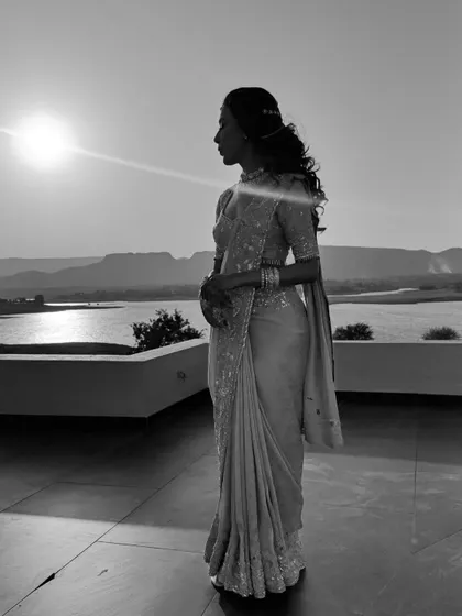 A black and white silhouette against the sunset. The simple, elegant drape of the saree creates a timeless and romantic image.