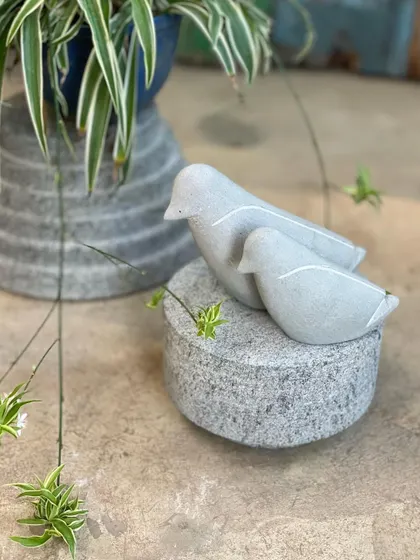 A pair of minimalist stone birds rest on one of our cylindrical granite plinths, showcasing a modern aesthetic.