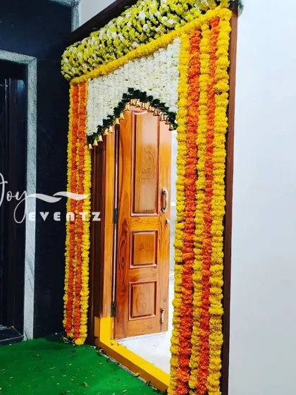 A traditional housewarming door decoration using garlands of orange and yellow marigolds and white jasmine. This classic design brings a festive and auspicious feel to your new home's entrance.