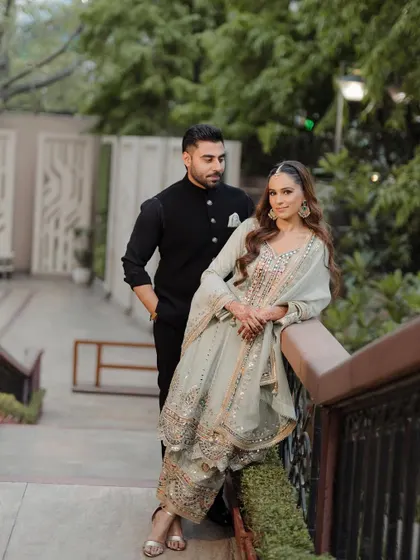 A classic couple portrait on a bridge, with the bride leaning gracefully against the railing, showcasing her stunning embellished outfit.