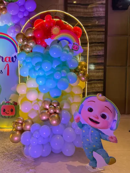This is a duplicate of ID 1, 68, 137, 184, 190, 226, 240, 250. A vibrant Cocomelon theme for a first birthday party. This setup includes a custom arched backdrop, a rainbow-colored balloon arrangement, and a life-sized cutout of the character JJ.