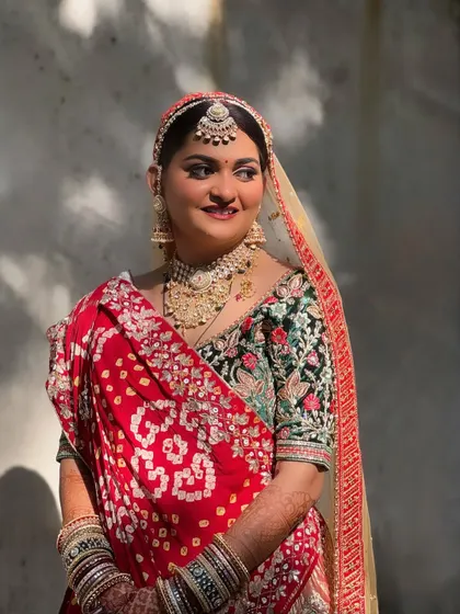 A beautiful Gujarati bride in a traditional red bandhani saree. The makeup is kept classic and radiant to complement the vibrant colors and heavy embroidery of her outfit.