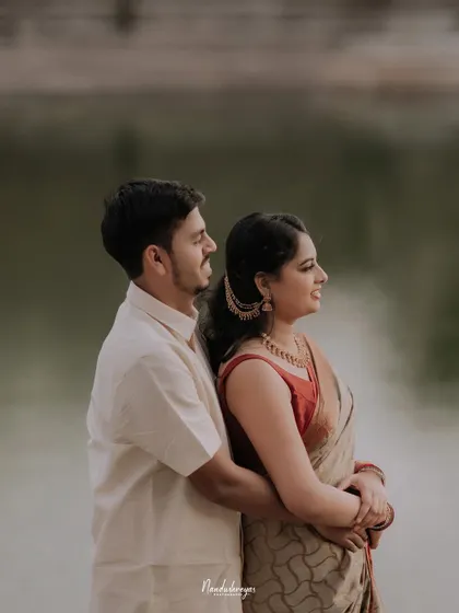 A couple stands by the water, the groom embracing the bride from behind as they both look out at the view, creating a calm and connected portrait.