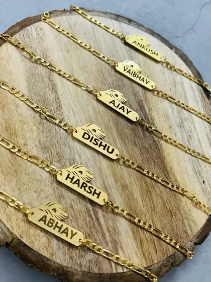 A collection of gold-plated chain rakhis with nameplates and feather charms.