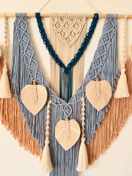A close-up of the central part of the blue and tan wall hanging, showing the intricate knot work and leaf details.