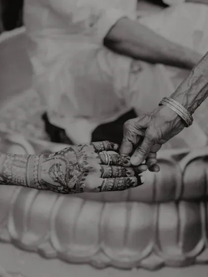 A powerful black and white photo of a young hand with intricate henna being held by an older, wrinkled hand, symbolizing the passing of blessings through generations.