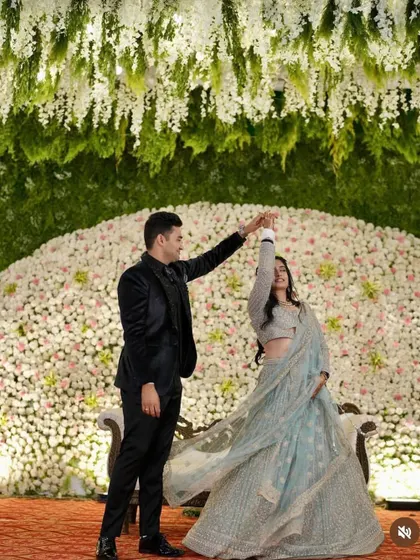 A couple dancing on their reception stage, set against a backdrop of thousands of white flowers and hanging floral installations.