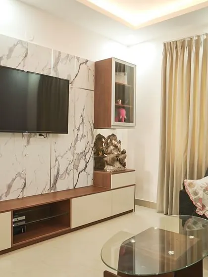 A modern living room with a TV unit set against a full-wall marble-finish panel. The simple wood and white console provides storage without overwhelming the space.