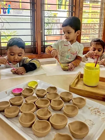 Toddlers sit at a table, focused on painting their clay diyas. This activity is a wonderful way to develop their concentration and creativity.