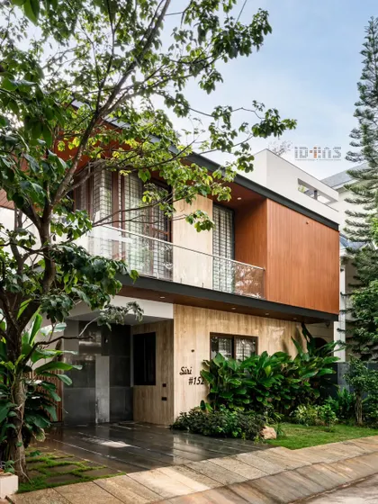 The completed Prakash Reddy residence, surrounded by lush landscaping. The design uses a mix of travertine marble and wood-finish cladding to create a warm, modern, and inviting exterior.