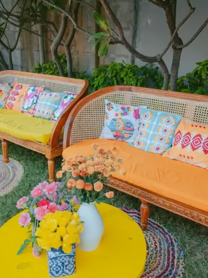 A vibrant lounge area with cane sofas, bright yellow and orange cushions, and colorful coffee tables.