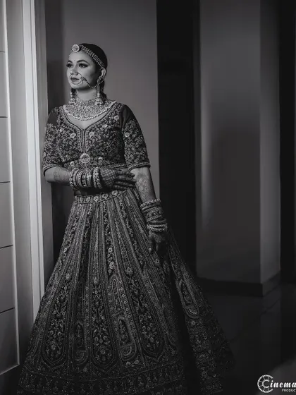 A classic black and white full-length bridal portrait, emphasizing her elegant posture and the intricate details of her lehenga.