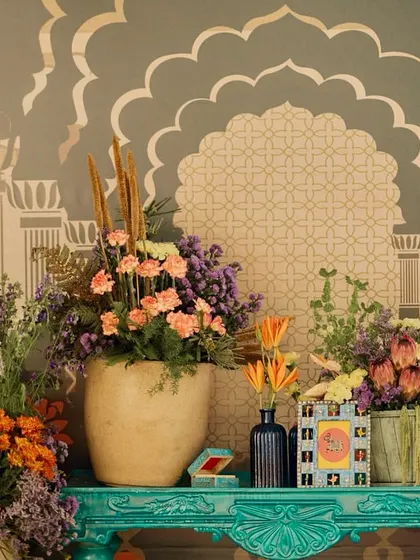 A beautiful floral arrangement on a turquoise console table, set against a wall with painted Rajasthani arch motifs.