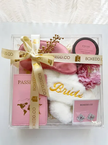 A clear shot of our acrylic bride-to-be hamper. This packaging allows the curated items inside, like the passport holder and embroidered slippers, to be the star of the show.
