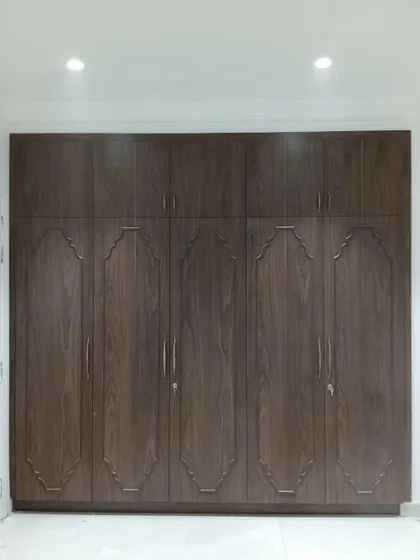 A full-height wardrobe in a dark wood finish with classic molding details on the shutters. This piece provides ample storage while adding a sense of traditional grandeur to the bedroom.