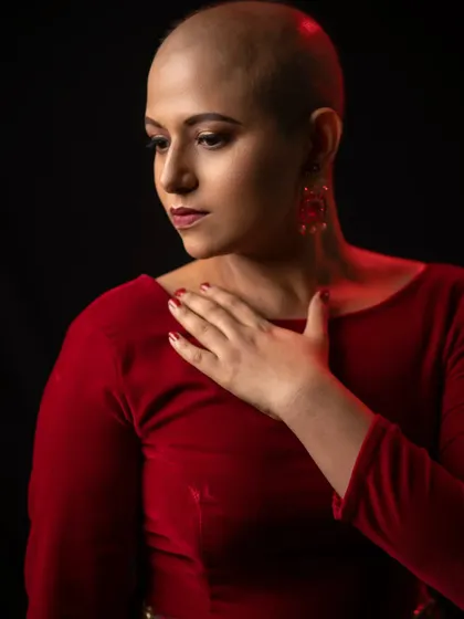 This image captures a moment of quiet confidence. The makeup is soft and warm, with a focus on flawless skin and a defined lip, perfectly complementing the rich red tones of the shoot.