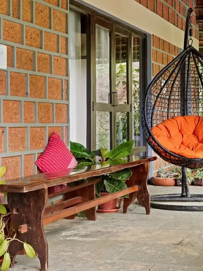 A relaxing spot on the veranda of Villa Magnolia, with a swing chair and a rustic wooden bench. The exposed laterite brick wall adds texture and a sense of place.