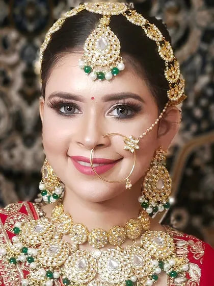 A happy bride smiling in a full Pachi Kundan set with green bead accents. This set includes a choker, matching earrings, maang tikka, and a simple, elegant nath.