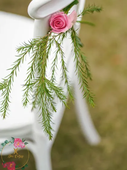 A single pink rose with greenery tied to a white chair, a simple yet elegant detail.