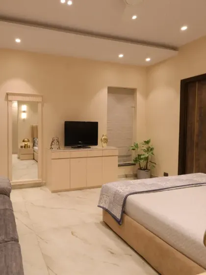 This view shows the functional layout of the mother's bedroom, with a simple TV unit, a full-length mirror, and a comfortable grey sofa.