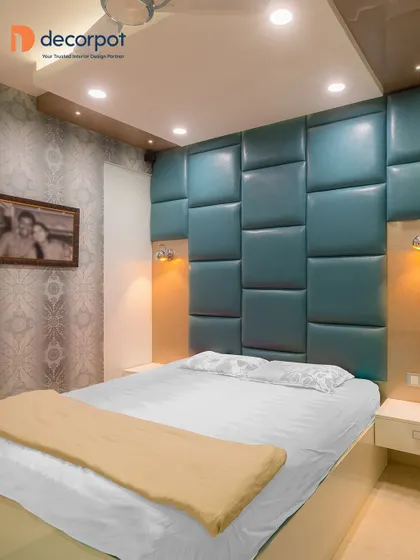 A luxurious bedroom featuring a floor-to-ceiling padded headboard in a striking teal color. The design creates a dramatic and comfortable focal point in the room.