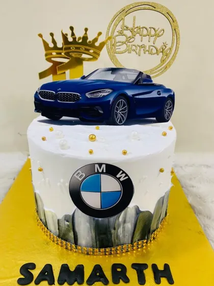 The ultimate driving machine, in cake form. A stylish BMW-themed cake with the logo, a blue convertible topper, and golden crowns.