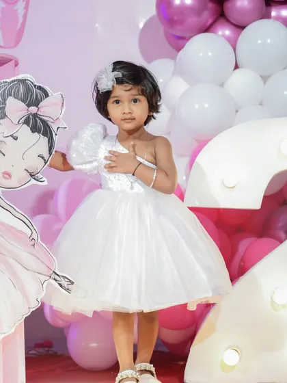 This shot highlights the details of the one-shoulder party dress, including the textured puff sleeve and the shimmering fabric of the bodice. It's a modern and chic choice for a stylish toddler.