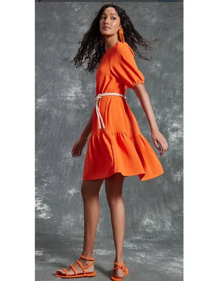 A bright and cheerful orange tiered dress styled for a summer collection. The movement of the dress and matching accessories create a fun, energetic vibe.
