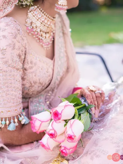 A detail shot of the bride, Ratika, holding a bouquet of pink-tipped roses that match her pastel lehenga.