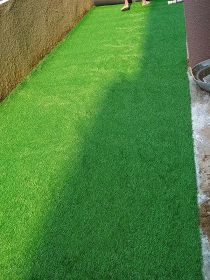 The artificial grass is laid out over the prepared base. The final steps involve securing the edges and brushing the fibers.