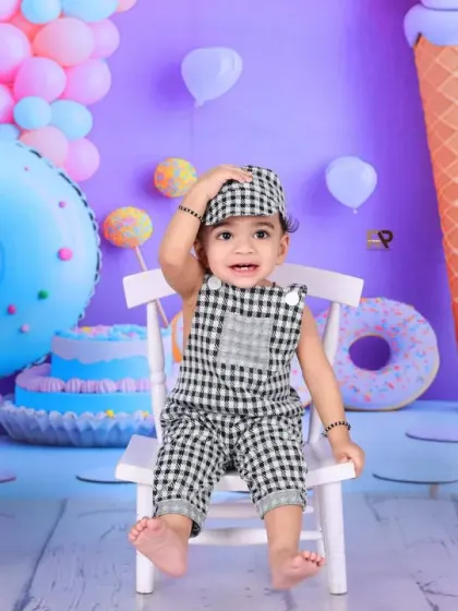 A baby boy strikes a pose in the sweet shop, looking absolutely adorable in his checkered outfit and cap. The pastel purple and blue backdrop is fun and eye-catching.