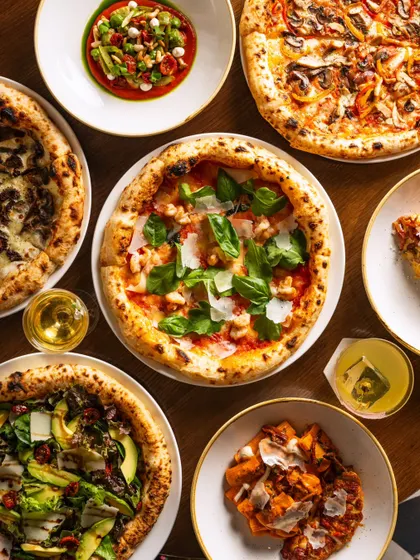 An overhead shot of multiple Neapolitan-style pizzas and appetizers. This "flat lay" style is highly effective for social media, showcasing variety and encouraging sharing.