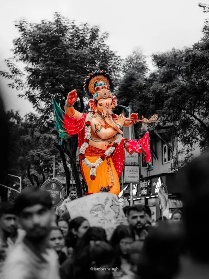 A powerful black and white photo with a splash of color, showing a Ganpati idol being carried through the streets of Mumbai. This editing style highlights the idol's vibrant presence amidst the devoted crowd.
