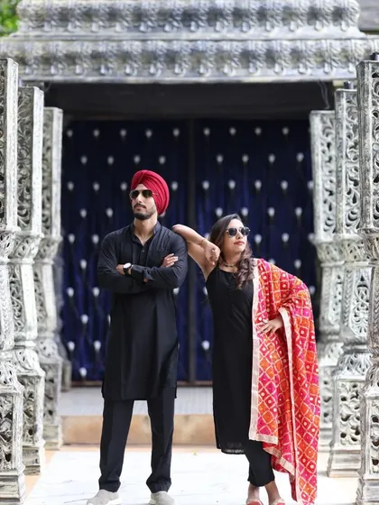 A modern and stylish portrait of a couple in matching black ethnic wear. Their confident poses and sunglasses give a cool, editorial vibe to this shot taken among carved pillars.
